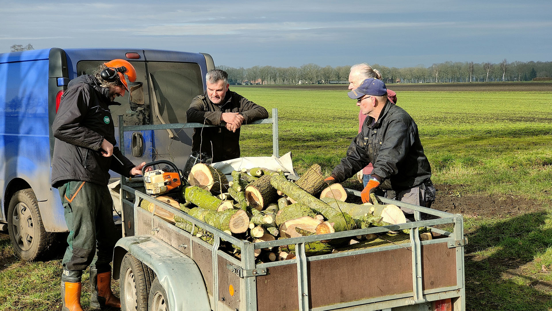 Groengroep mensen bij een wagen vol met boomstammen en takken